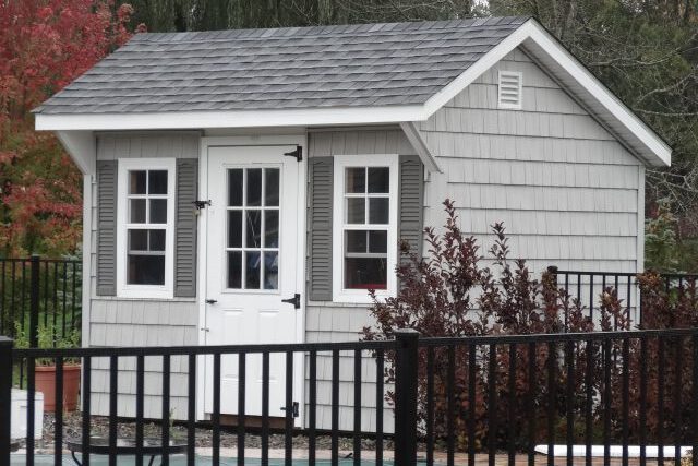 A small cottage-style garden shed behind a black fence