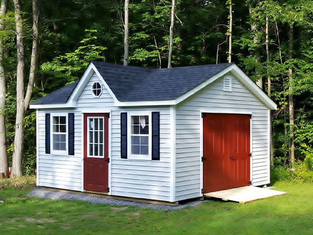 A New England-style cottage shed with bright red doors in a grassy area 